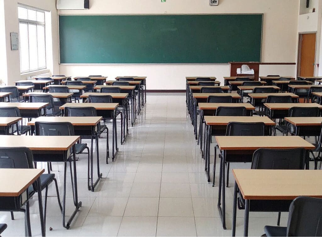 Empty classroom with rows of desks and a large green chalkboard.