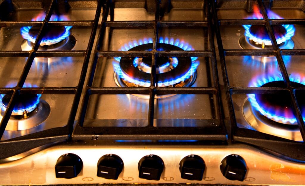 A gas stove burner lit with blue flames under a metal grate.