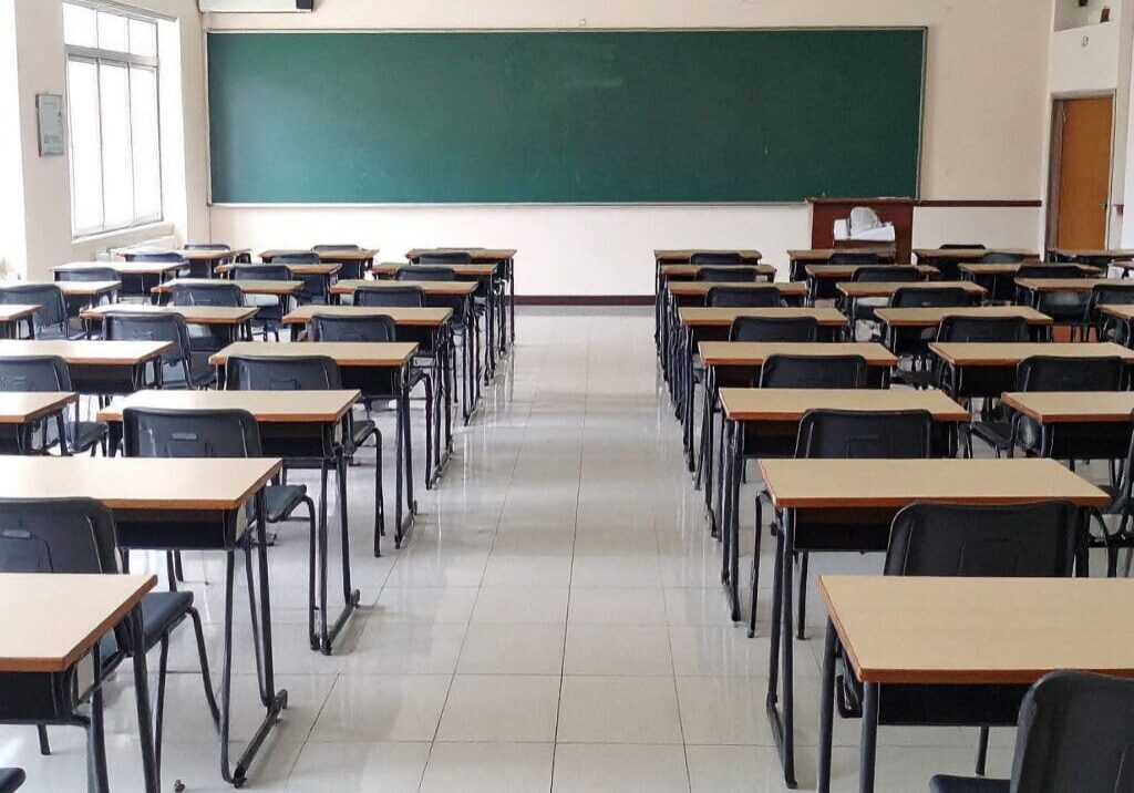 Empty classroom with rows of desks and a large green chalkboard.