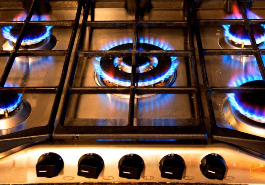 A gas stove burner lit with blue flames under a metal grate.